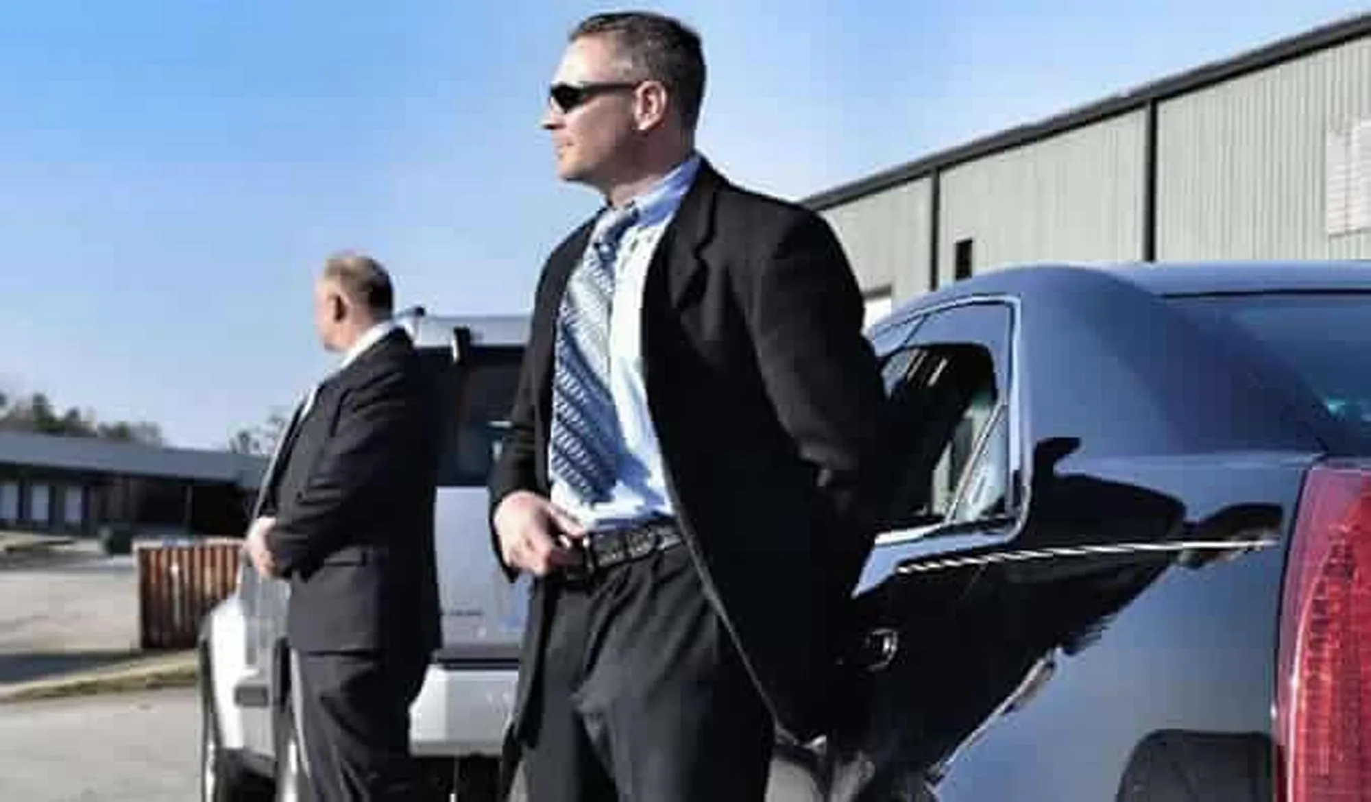 Protective agent in sunglasses standing beside a vehicle for a VIP principal