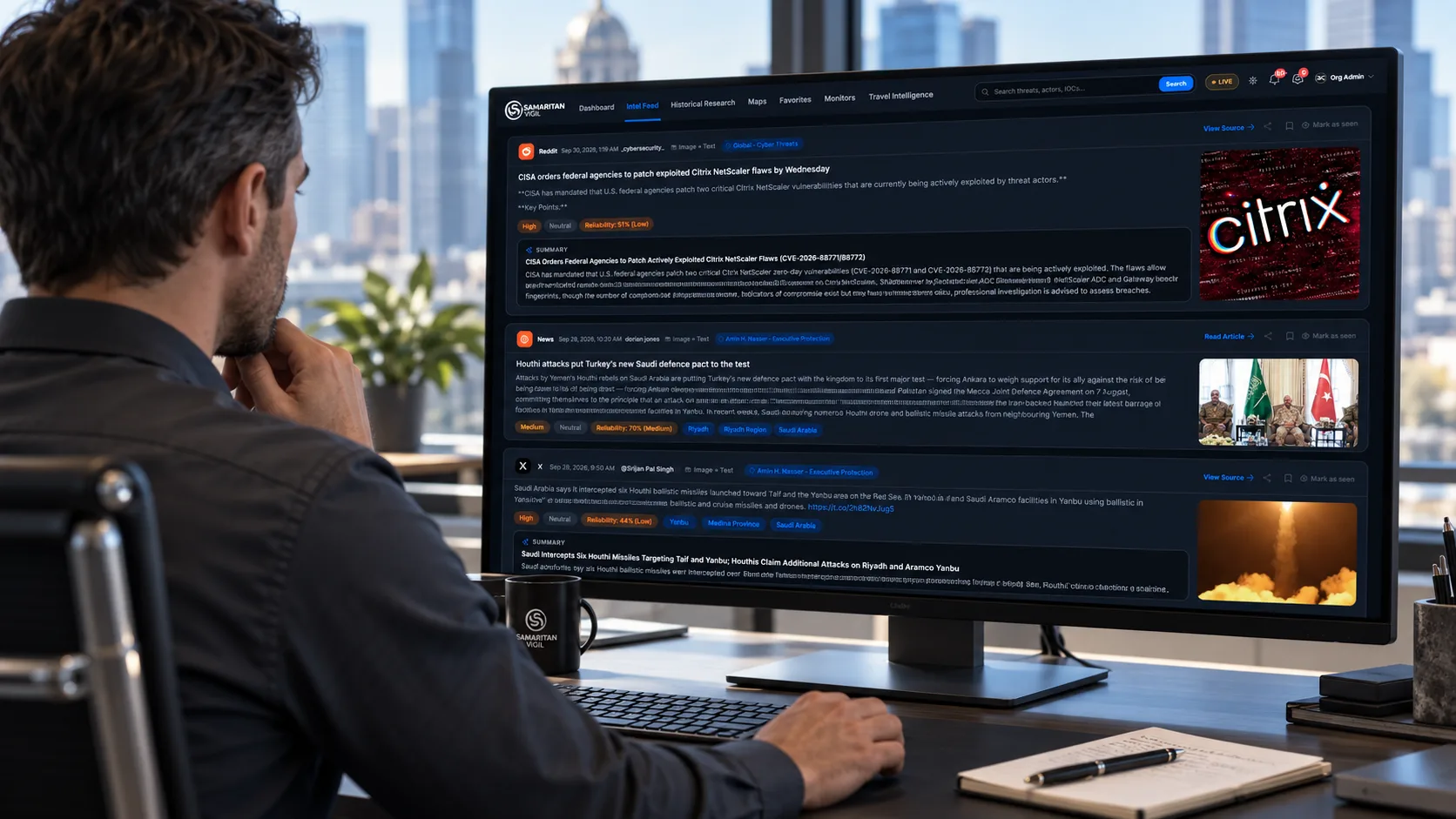A security analyst at a desk reviews the Samaritan Vigil™ Intel Feed on a large monitor, showing source-tagged updates with threat-level and reliability ratings and AI-generated summaries.